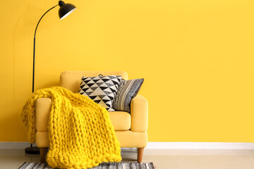 Armchair with blanket and stack of pillows near yellow wall