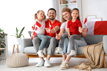Obraz premium Happy family with flags of Canada sitting on sofa at home