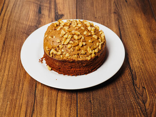 A dessert cake in brown color with nuts in a plastic container on a wooden table. Bakery product, party food. Tasty snack.