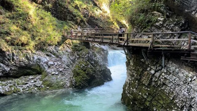 A bridge over a river with a waterfall in the background. The bridge is wooden and he is old