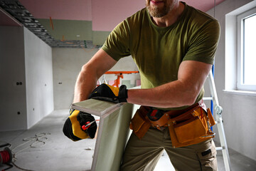Construction worker carefully cutting drywall using a utility knife, prioritizing safety and...