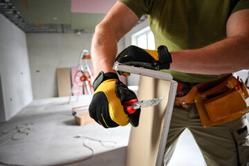 Construction worker carefully cutting drywall using a utility knife, prioritizing safety and precision on a home renovation project