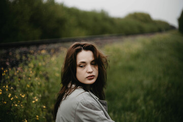 Naklejka premium beautiful woman in a gray coat posing in nature in cloudy weather, gloomy mood.