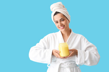Beautiful young happy woman in bathrobe with jar of cosmetic product on blue background