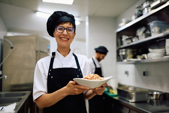Happy female chef working in restaurant kitchen and looking at camera.