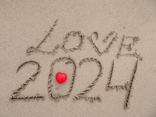 Sign love and 2024 on a sand of a beach and read heart. Top down view