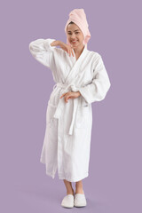 Beautiful young happy woman in bathrobe with towel on purple background