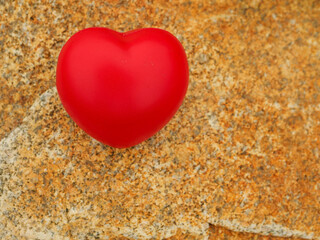 A red heart is sitting on a rock. The heart is small and red, and it is placed on a brown surface. Concept of love and warmth, as the heart is a symbol of affection and care. Copy space for a message