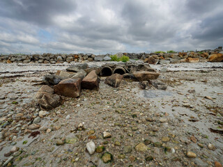 Water drain pipes on a rocky beach, stone fence in the background and blue sky. Sewage in a nature environment. Ireland, county Galway. Ecology issue