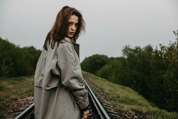 gloomy woman in a gray coat walks along the railway, concept of depression and sadness in crisis