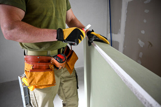 Construction worker wearing tool belt and holding drywall and utility knife preparing to cut