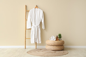 Decorative ladder with cosmetic products and hanging bathrobe near beige wall