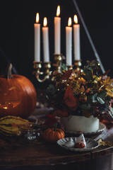 Homemade delicious chocolate cake with coloured orange cream and meringue ghosts, pumpkins for Halloween home party. Elegant beautiful table arrangement with candles, chandelier, Jack-o-Lantern