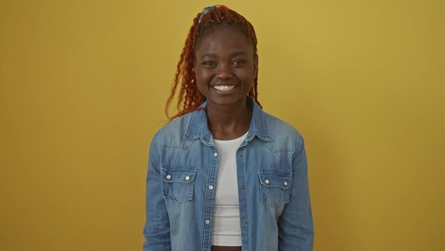 Fun, comical african american woman wearing denim shirt, making a fish face expression; standing over an isolated yellow background showcasing her crazy, funny nick in a silly gesture with lips