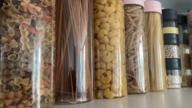 A row of clear containers filled with various types of pasta and grains on shelf