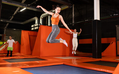 Excited active woman enjoying moment of freedom and fun while jumping at well-equipped indoor trampoline arena..