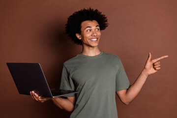 Photo portrait of young guy in gray t shirt remote holding netbook point finger developing store online isolated on brown color background