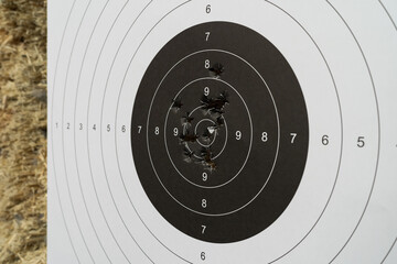 A shooting paper target with bullet holes in the center in a shooting range on a wooden bullet...