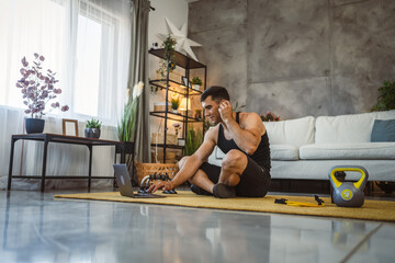 Young man with earphones take a break from training and use laptop