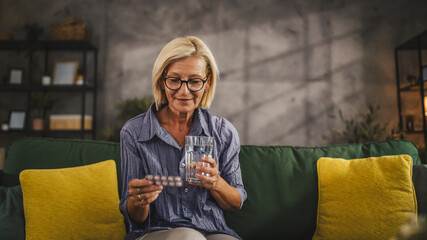 Mature woman drink the medicine with glass of water at living room