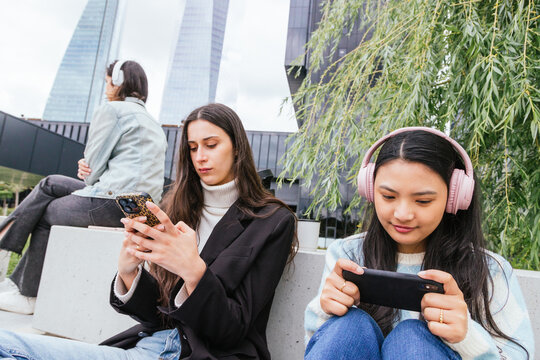 Three students using technology outdoors in urban setting - Powered by Adobe