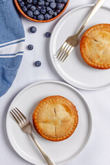Two mini blueberry pies on the white plates, overhead view