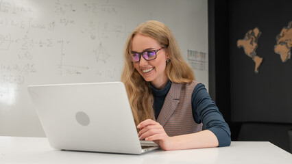 Caucasian woman scientist typing on laptop. White board with formulas. 