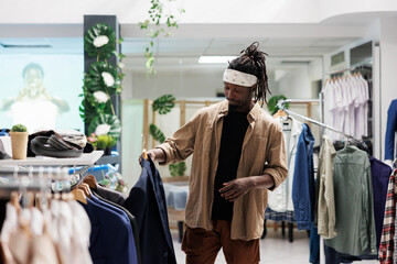 African american man browsing casual shirts in clothing store. Customer holding trendy apparel on hanger and checking outfit style before makeing purchase in shopping mall