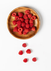 Top view of fresh raspberries in a wooden bowl on a white background. The vibrant red berries create a striking contrast against the natural wood and clean surface, ideal for healthy eating