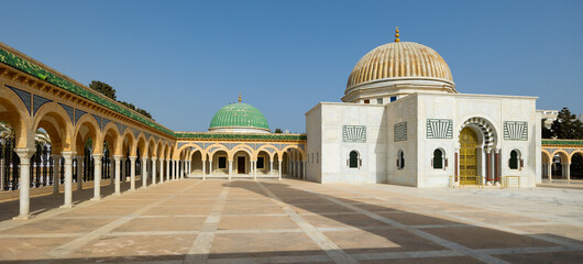 Scenic view of Habib Bourguiba Mausoleum in Tunisian city of Monastir with green and gold domes and sun-drenched vast courtyard framed by elegant archways