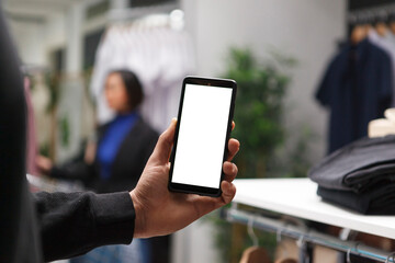 Shopping mall buyer hand holding smartphone with empty screen, browsing apparel online and in boutique. Clothing store customer using mobile phone with blank touchscreen mockup for promotion