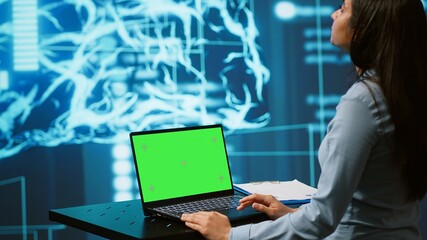 Startup employee looking over charts, using AI software on green screen laptop to take data driven...