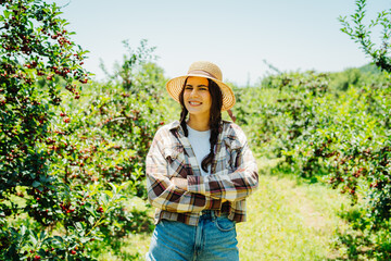 One young caucasian girl with a straw hat in cherry field checking on trees and cherries on a sunny day	