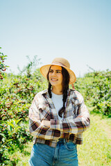 One young caucasian girl with a straw hat in cherry field checking on trees and cherries on a sunny day	