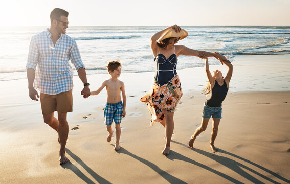 Happy family, playing and holding hands with children on beach sunset for summer holiday or bonding together in nature. Mother, father and kids with smile for stroll or outdoor weekend by sand shore