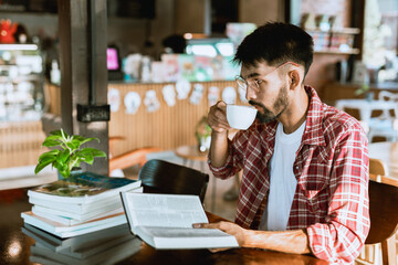 Portrait of a bearded Asian man wearing glasses. Drinking coffee and reading at a coffee shop