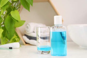 Bottle of mouthwash and glass on white table in bathroom