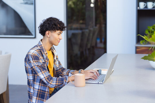 Using laptop at home, teenage boy working with coffee mug on table, copy space