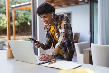 Using smartphone and laptop, teenage boy multitasking at home office © wavebreak3