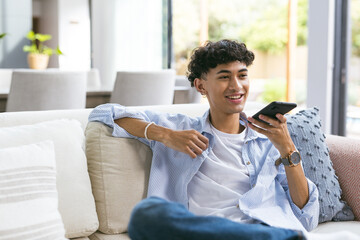 Relaxing on couch, teenage boy using smartphone and smiling at home