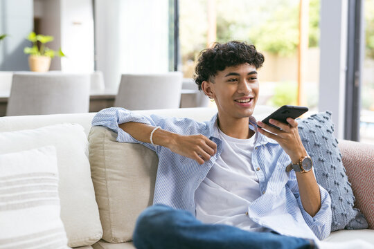 Relaxing on couch, teenage boy using smartphone and smiling at home