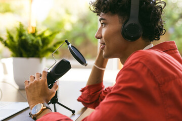 Recording podcast, young man with headphones speaking into microphone at home - Powered by Adobe