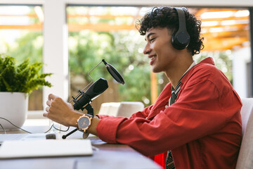 Recording podcast, teenage boy with headphones speaking into microphone at home