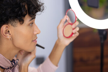 Applying makeup, transgender transgender woman using compact mirror and brush at home