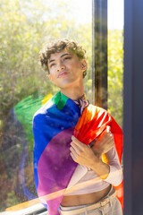 Wearing rainbow flag, transgender transgender woman standing by window, looking outside