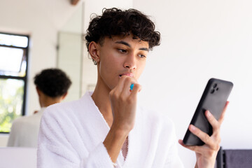 Brushing teeth, young young man in bathrobe using smartphone in bathroom