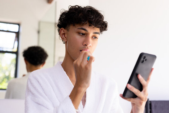 Brushing teeth, young young man in bathrobe using smartphone in bathroom - Powered by Adobe