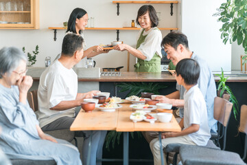 お手伝いする子供と家族に料理をふるまう主婦・ママ・母親と三世代家族
