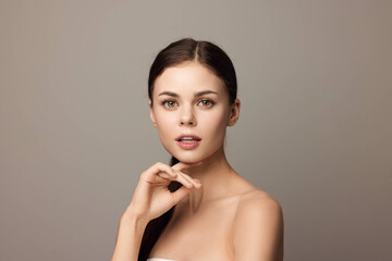 Beautiful young woman posing with hands on chin, looking at camera, closeup on gray background
