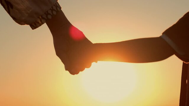 Mom and child holding hands together on sunset background. Mother son silhouette